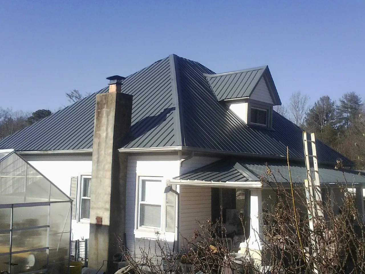 Dark blue standing seam metal roof on a white farmhouse with dormer — Slate & Tile Roof Repair by Roofing Brothers in Genesee