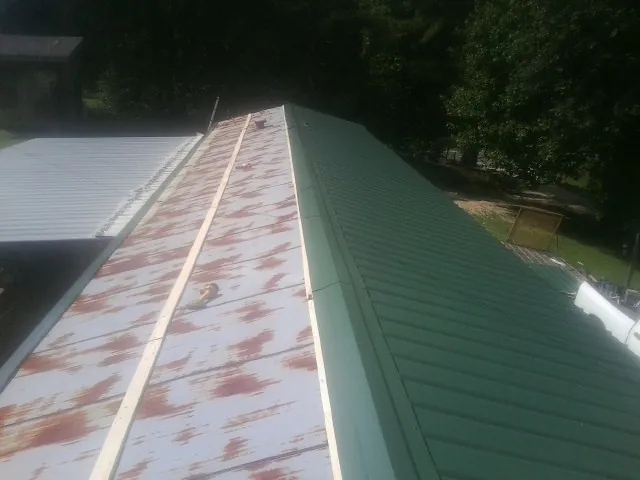 Old rusted panels beside newly installed green metal roofing — Wind Damage Roof Repair by Roofing Brothers in Genesee