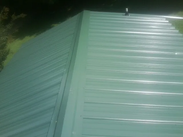 New green metal panels meeting at the ridge of a roof — Flat Roof Repair work by our crew in Genesee