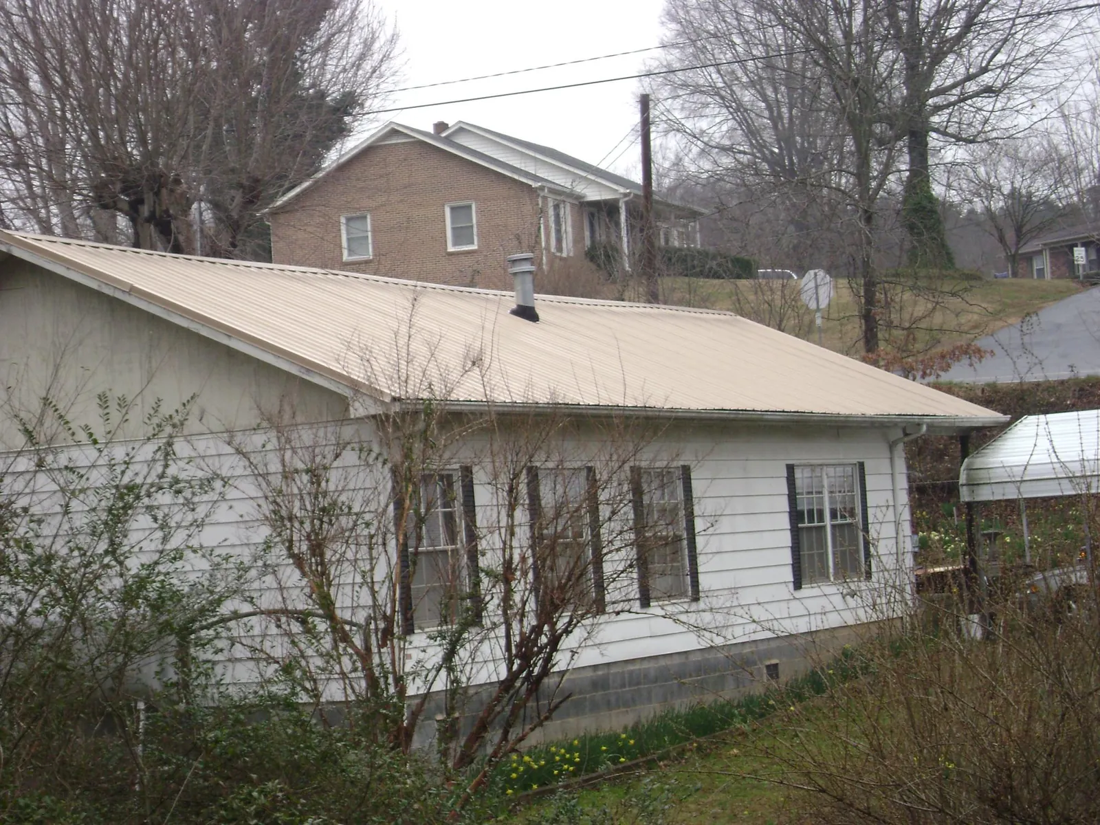 Tan metal roof on a white sided house set into a hillside — Commercial Roofing by Roofing Brothers in Genesee