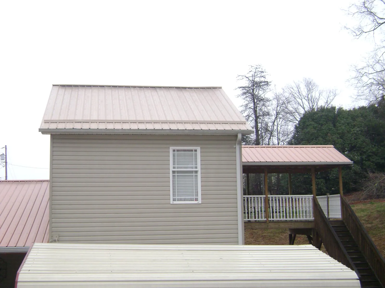 Tan metal roofs on a two story addition and attached porch, from a Roof Replacement job in Genesee